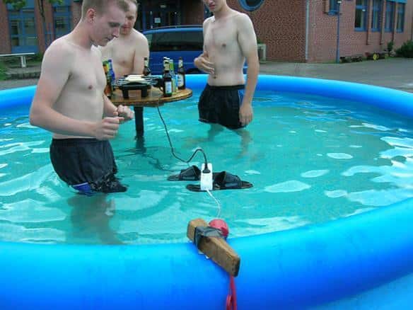 êtres irrationnels : 3 jeunes hommes dans une piscine avec une multiprise électrique branchée flotant sur 2 tongues